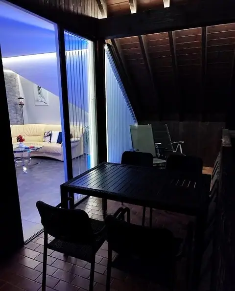 Balkon am Abend, durch die Glastür ist das Wohnzimmer zu sehen