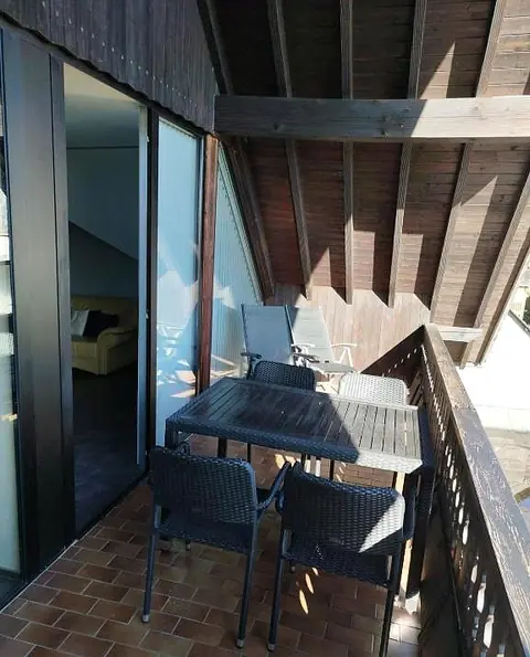 Überdachter Holzbalkon mit Tisch und vier Stühlen