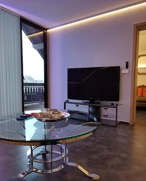 Wohnbereich mit Fernseher, rundem Glastisch und Tür zum Balkon